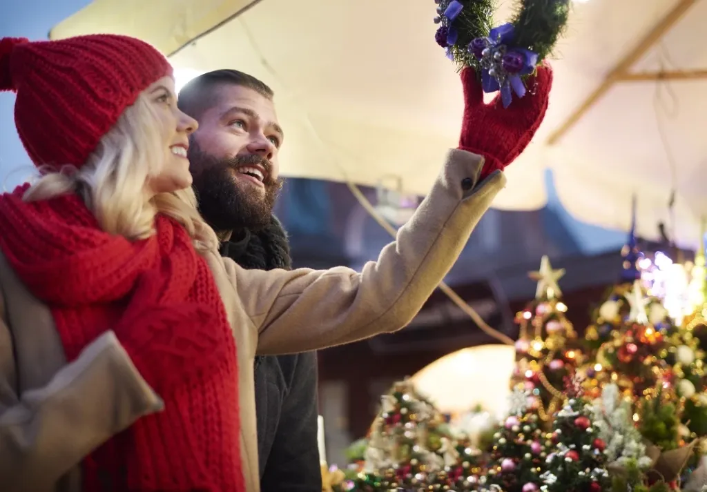 Paar betrachtet am Christkindlmarkt einen Adventskranz mit blauen Kerzen