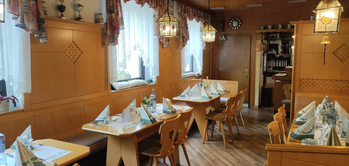 Kleines Gastzimmer mit eingedeckten Tischen, Holzvertäfelung und gemütlicher Beleuchtung