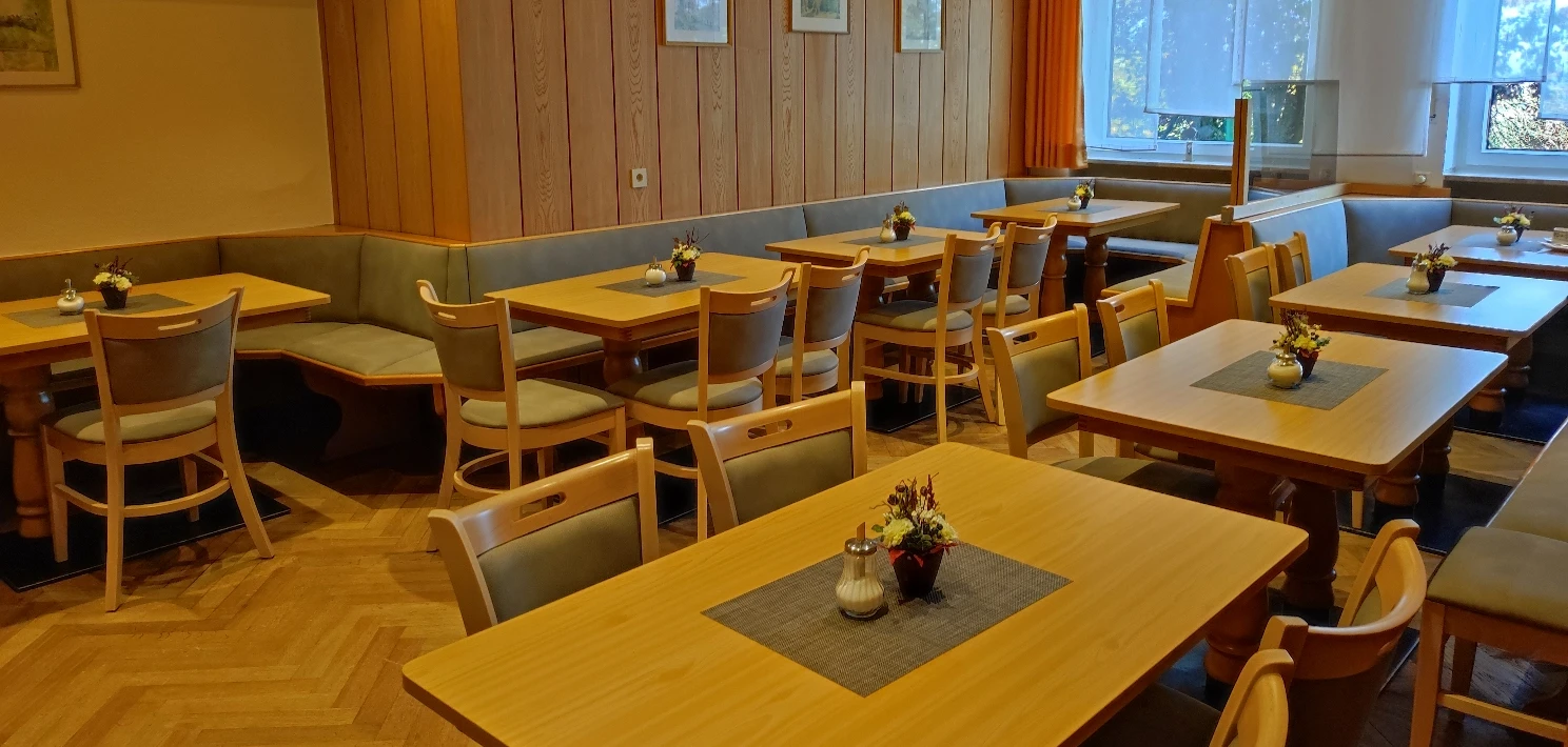 Frühstückszimmer mit Holzvertäfelung, Sitzbänken und gedeckten Tischen auf Parkettboden