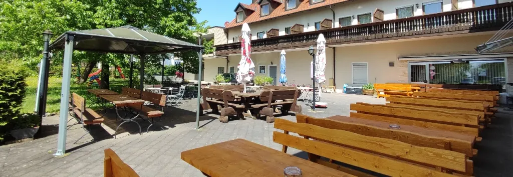 Sonniger Biergarten mit Holztischen und Bänken vor dem Hotel-Gasthof