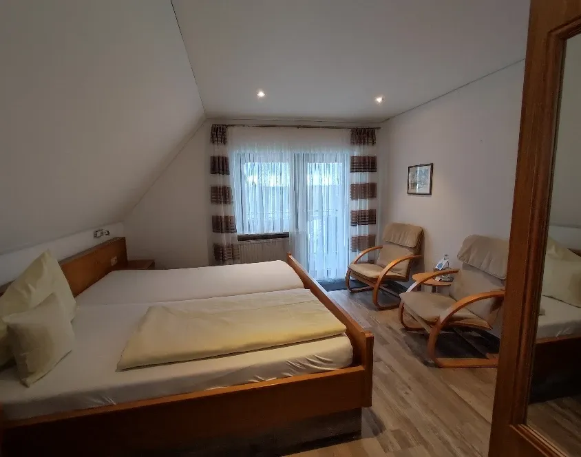 Doppelzimmer mit Holzbett, zwei Sesseln, Dachschräge und Balkonfenstern