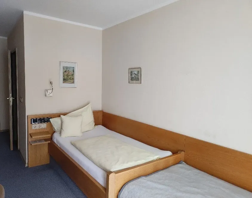 Einzelzimmer mit Holzbett, Nachttisch und gerahmten Wandbildern
