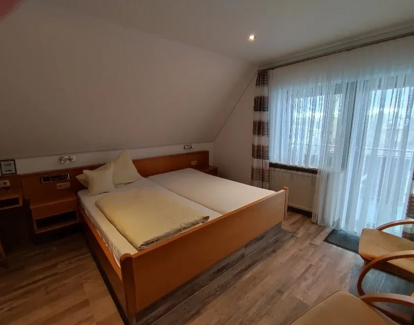Doppelzimmer mit großem Holzbett, Dachschräge und Balkonfenster mit Vorhängen