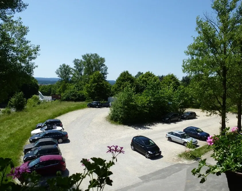 Hauseigener Parkplatz mit parkenden Autos, umgeben von Bäumen und Hügellandschaft