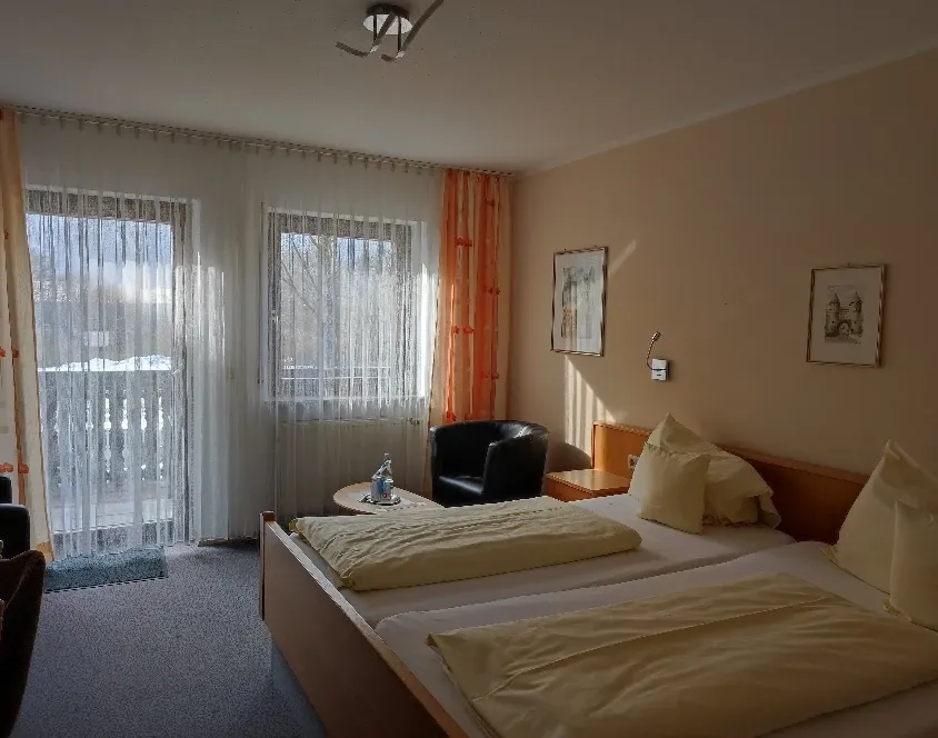 Doppelzimmer mit Bett, Sessel, Balkontür und Wandbildern in warmen Farben