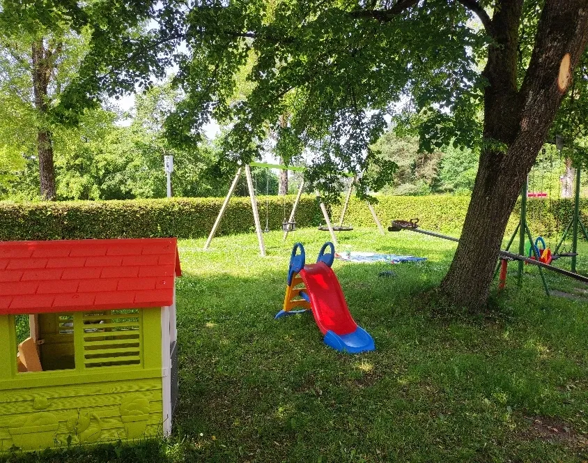 Spielplatz mit Spielhaus, Rutsche und Schaukel auf der Wiese unter Bäumen