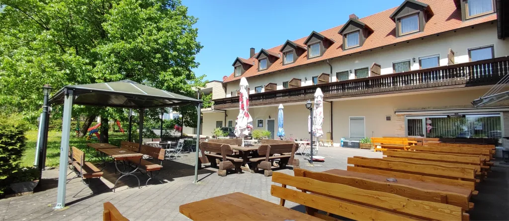Biergarten mit Holzbänken, Pavillon und Sonnenschirmen vor dem Hotel-Gasthof