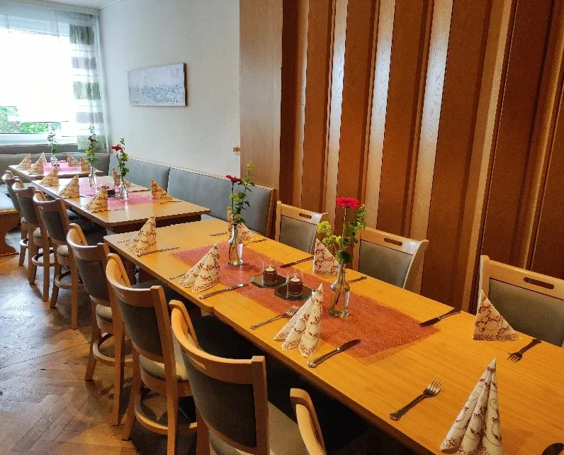 Frühstückszimmer mit eingedeckter Tafel und roten Blumengestecken