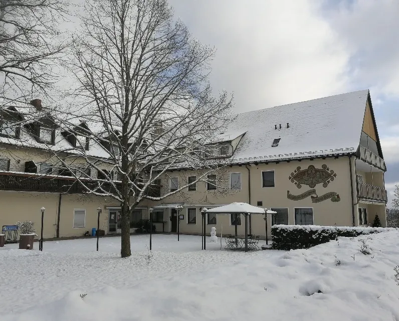 Hotel-Gasthof im Winter mit verschneitem Biergarten und kahlem Baum im Vordergrund