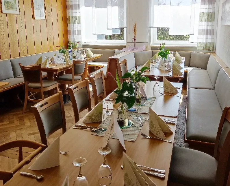 Frühstückszimmer mit gedeckten Tischen, Sitzbank und hellen Vorhängen