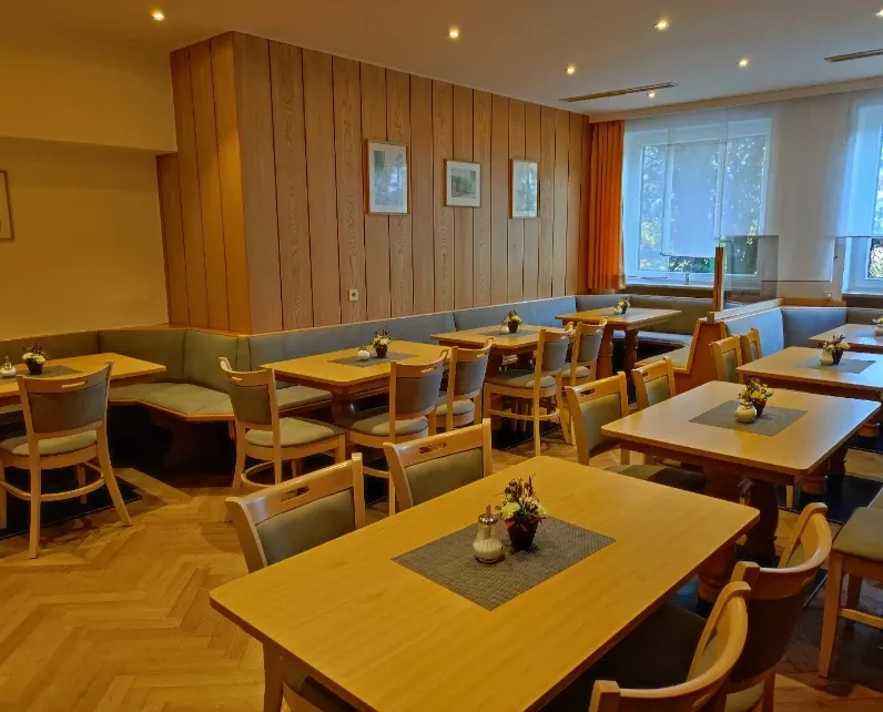 Frühstückszimmer mit Holzvertäfelung, Tischen mit Blumengestecken und Parkettboden