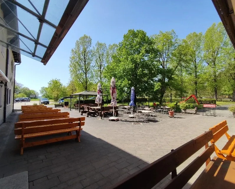 Blick aus der Terrasse auf den Biergarten mit Bäumen und Spielgeräten im Frühling