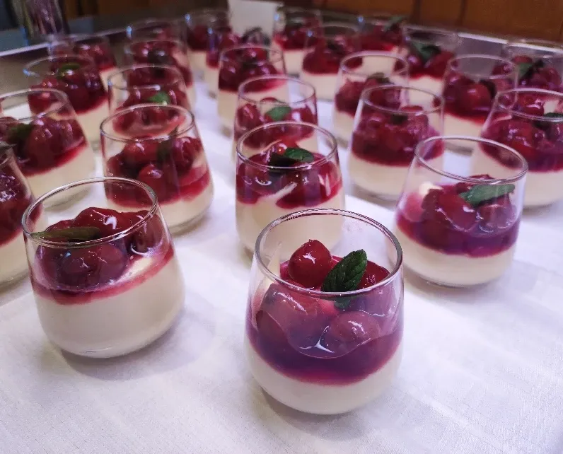 Reihen von Dessertgläsern mit Vanillecreme und Kirschen, dekoriert mit Minze
