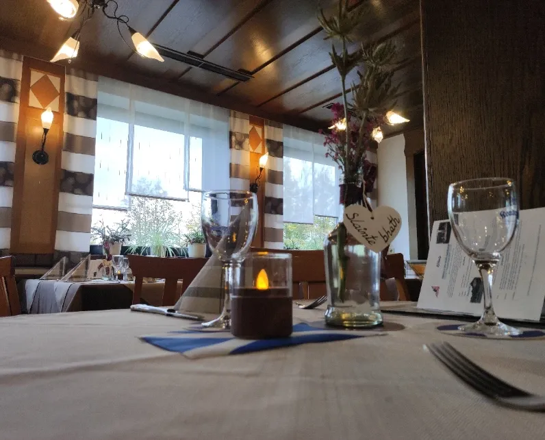 Tischdetail im großen Gastzimmer mit Weinglas, LED-Kerze und Holzherz an Blumenvase
